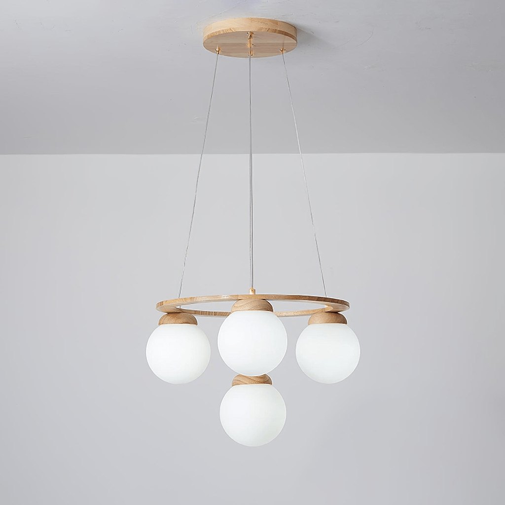 A smaller Clérachic chandelier with four frosted white globes under a light wood ring, hung from a wood plate against a grey wall.