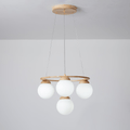 A smaller Clérachic chandelier with four frosted white globes under a light wood ring, hung from a wood plate against a grey wall.