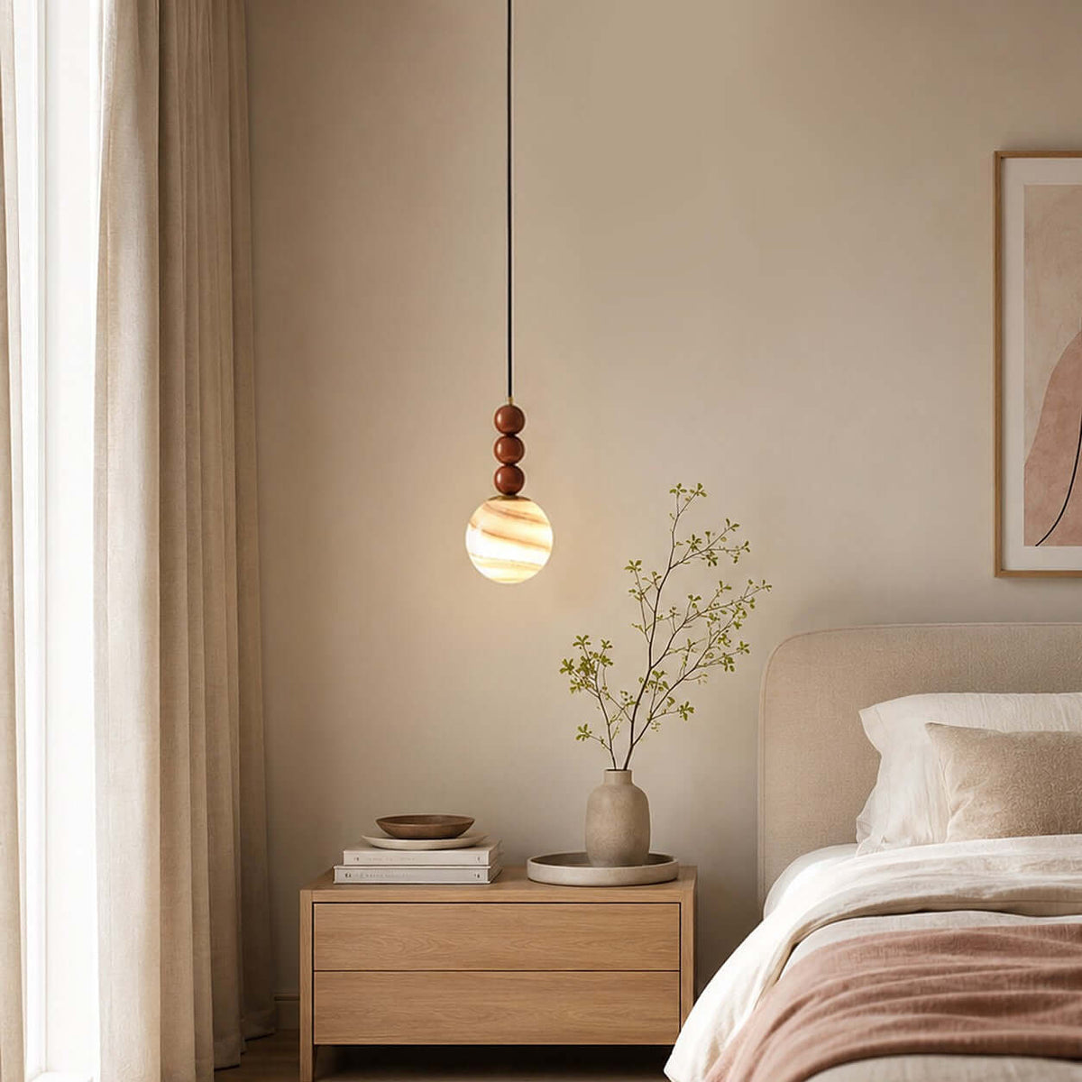 A glowing striped globe on a Clérachic pendant hangs beside a bed, with an oak bedside table and a sprig in a vase.