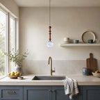 This Clérachic pendant with a pale blue marbled globe hangs over a kitchen sink with a brass tap and navy cabinets.