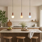 Three Clérachic pendants over a kitchen island: a white globe, a striped one and a blue one, all with turned wood stems.