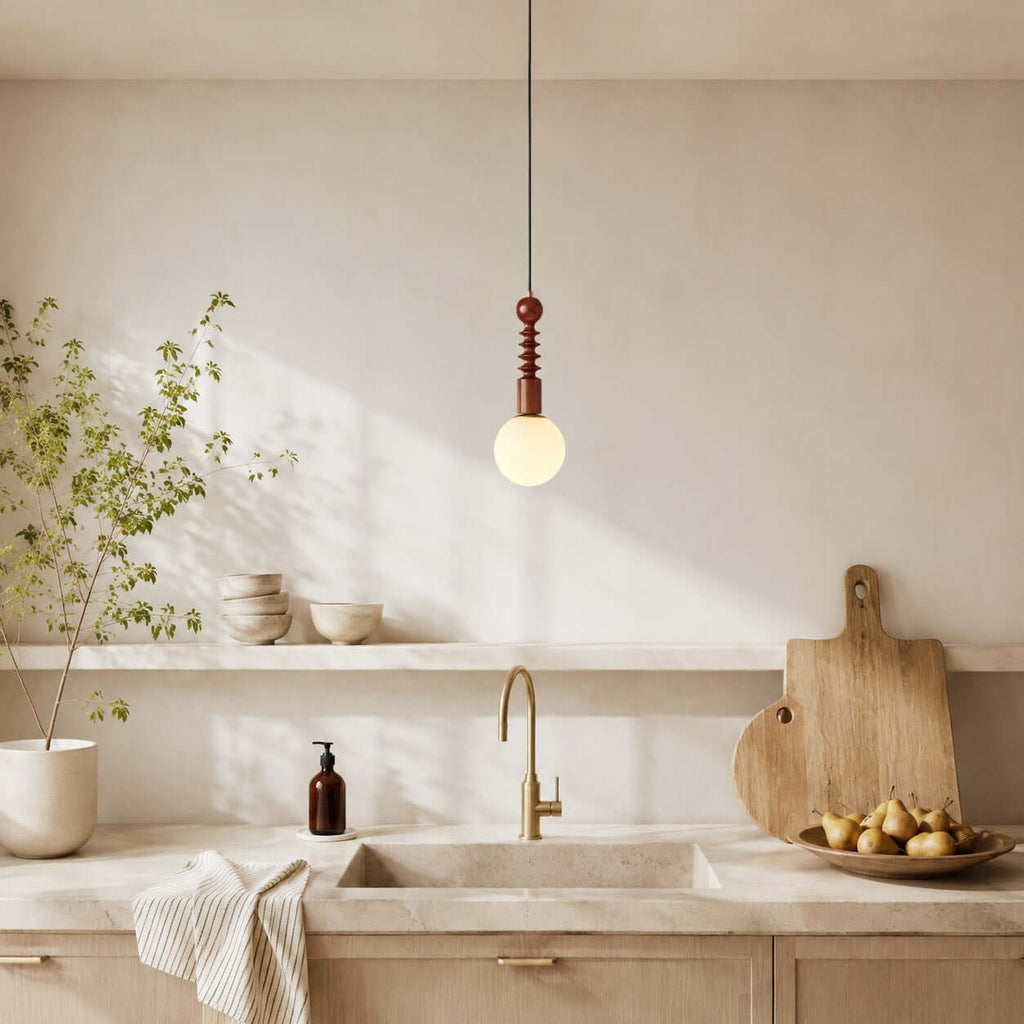 A white-globe Clérachic pendant with a turned wood stem hangs above a cream kitchen sink and a wooden chopping board.
