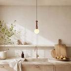 A white-globe Clérachic pendant with a turned wood stem hangs above a cream kitchen sink and a wooden chopping board.