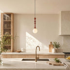A single Clérachic pendant with a frosted white globe hangs in a bright kitchen with oak cabinets and a stone worktop.