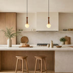Two Clérachic pendants with softly striped globes hang above an oak-fronted kitchen island with two wooden stools.