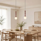 A pair of white-globe Clérachic pendants hangs over a light wood dining table with woven-seat chairs and a plant.