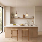 Two Clérachic pendants with white globes hang in a calm kitchen above an island with two rush-seat stools.