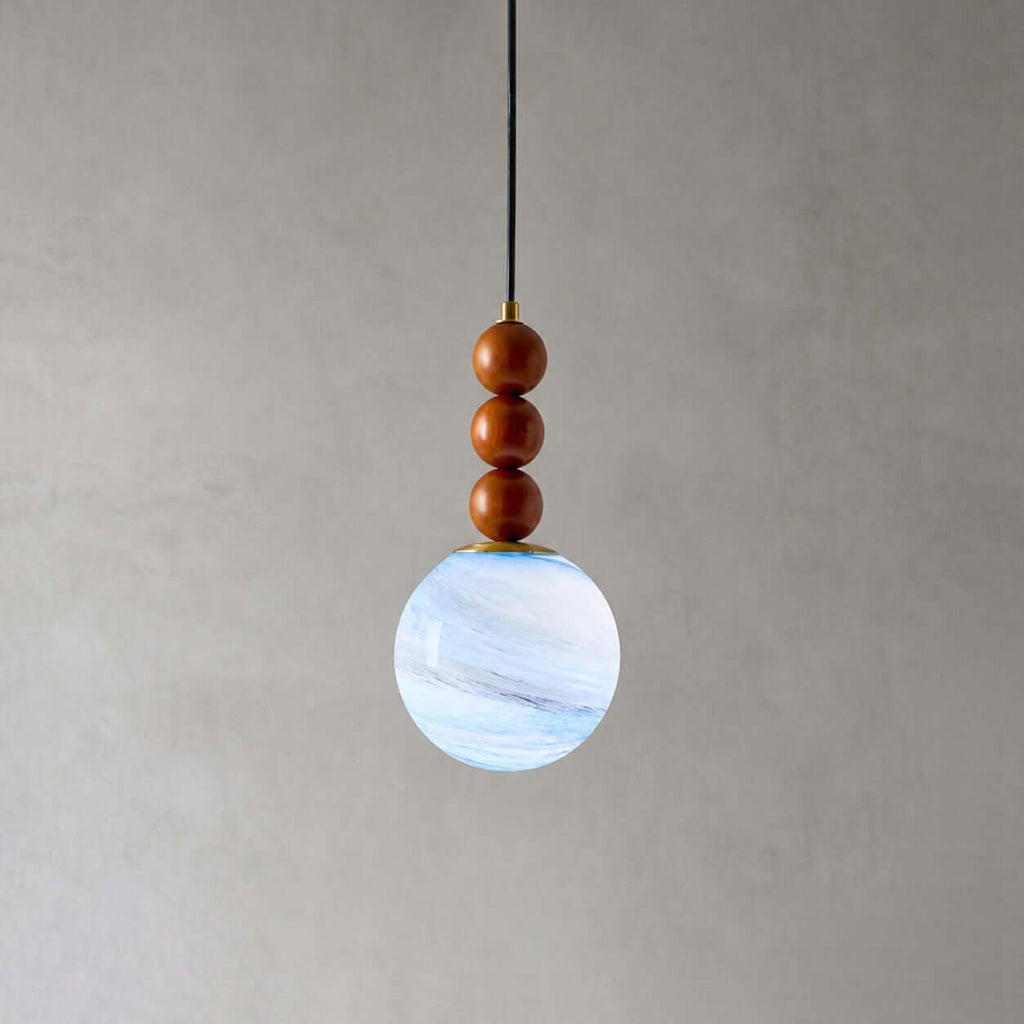 Close view of the three wooden beads and blue-white marbled globe on this Clérachic pendant, against a grey wall.