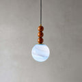 Close view of the three wooden beads and blue-white marbled globe on this Clérachic pendant, against a grey wall.