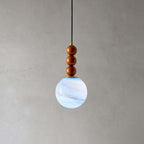 Close view of the three wooden beads and blue-white marbled globe on this Clérachic pendant, against a grey wall.