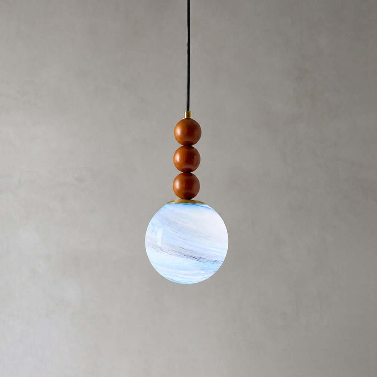 Close view of the three wooden beads and blue-white marbled globe on this Clérachic pendant, against a grey wall.