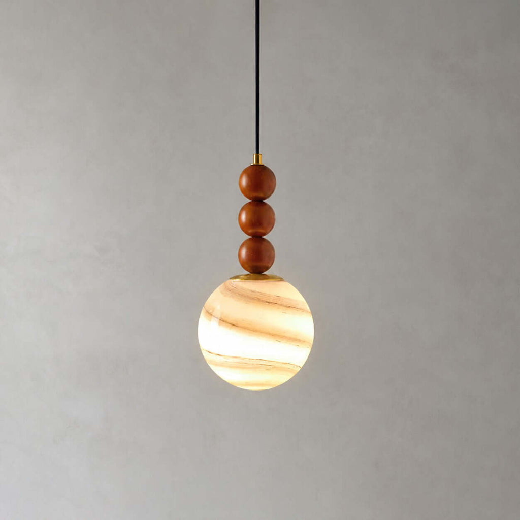 This Clérachic pendant has three wooden beads and a globe striped in cream and amber, glowing on a grey backdrop.