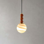 This Clérachic pendant has three wooden beads and a globe striped in cream and amber, glowing on a grey backdrop.
