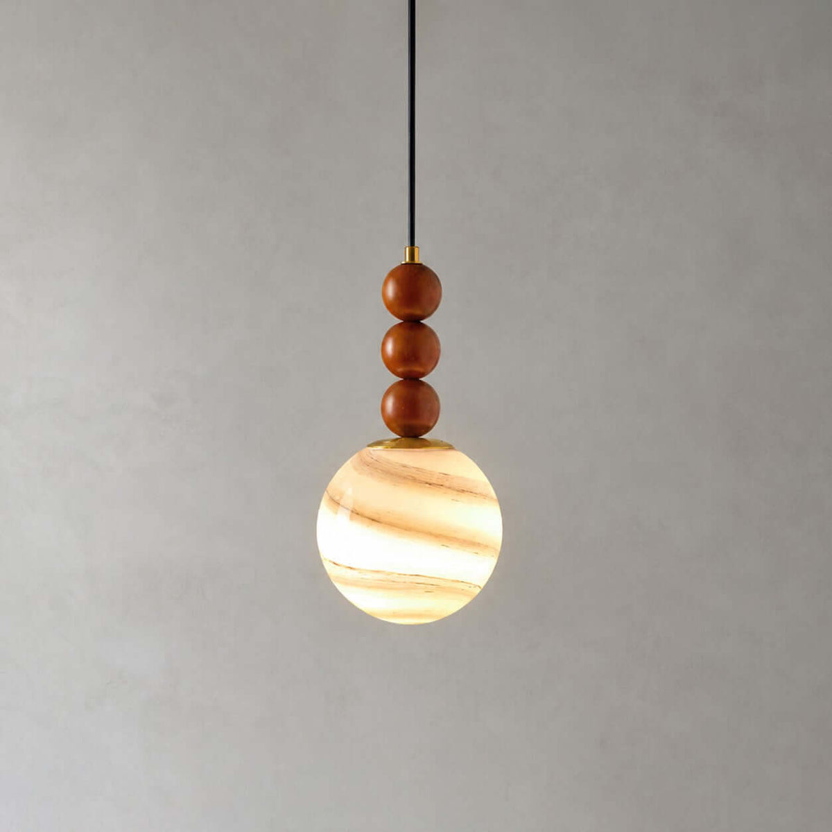 This Clérachic pendant has three wooden beads and a globe striped in cream and amber, glowing on a grey backdrop.