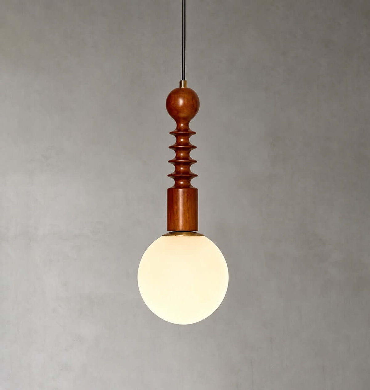 A frosted white globe glows beneath the ribbed wooden stem of this Clérachic pendant, against a textured grey wall.