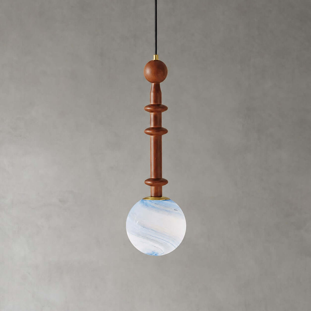 A slim wooden stem with two flat discs holds the pale blue swirled globe of this Clérachic pendant on a grey wall.