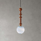 A slim wooden stem with two flat discs holds the pale blue swirled globe of this Clérachic pendant on a grey wall.