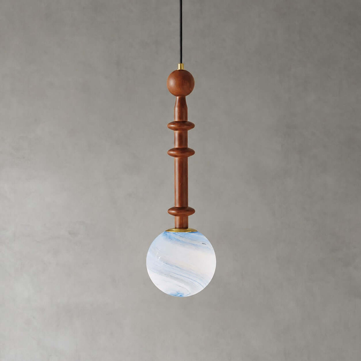 A slim wooden stem with two flat discs holds the pale blue swirled globe of this Clérachic pendant on a grey wall.