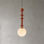 This Clérachic pendant has a slim turned wooden stem and a frosted white globe, lit warmly against a grey wall.