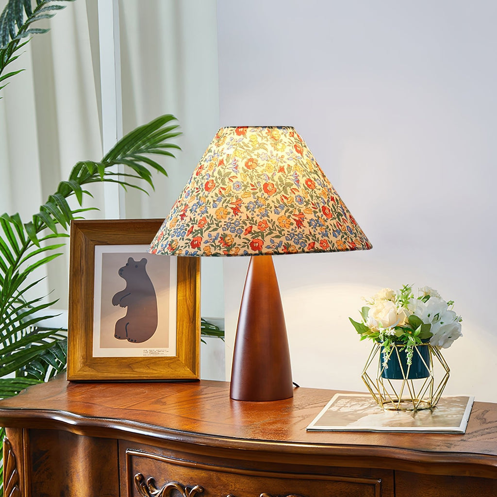 Floral-shaded Clérachic table lamp on a carved wooden sideboard, beside a framed bear print, a green plant and a gold basket of white flowers.