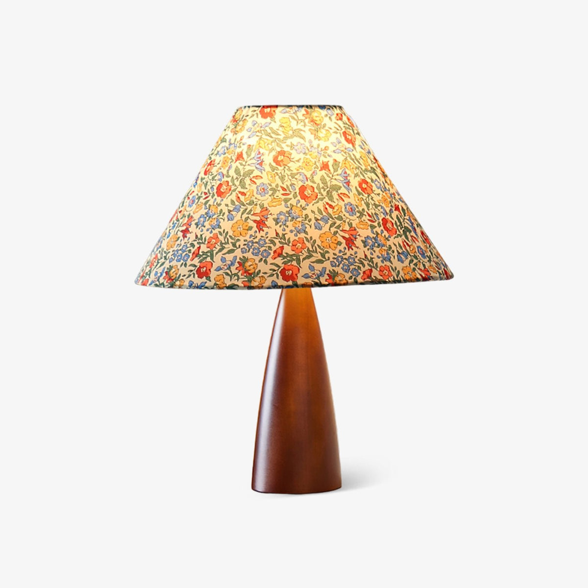 Clérachic table lamp with a wide conical shade in a small multicolour floral print on a smooth tapered wooden base, on a plain white backdrop.