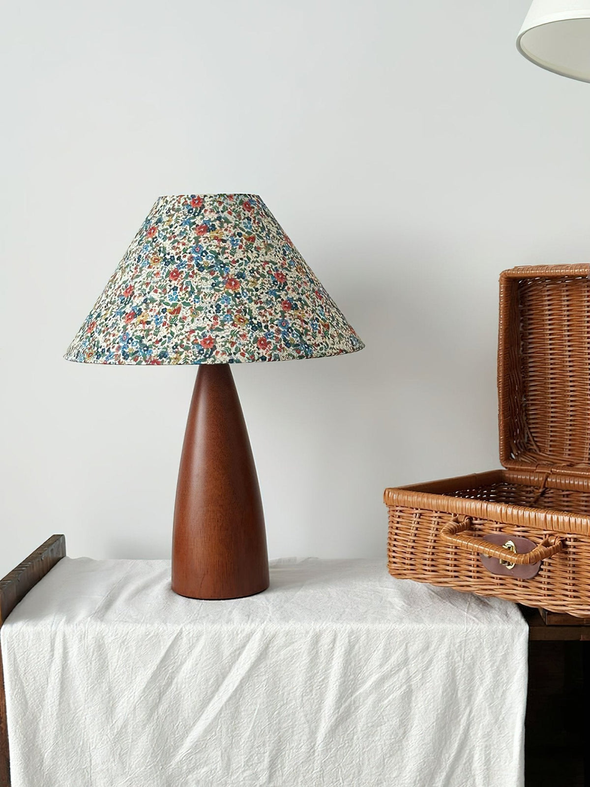 Unlit Clérachic table lamp on a white cloth, its blue-and-orange floral shade tilted slightly, beside an open wicker picnic basket.