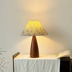Lit Clérachic table lamp on a white cloth-covered stand against a pale wall, its shade glowing yellow in a soft circle of light.