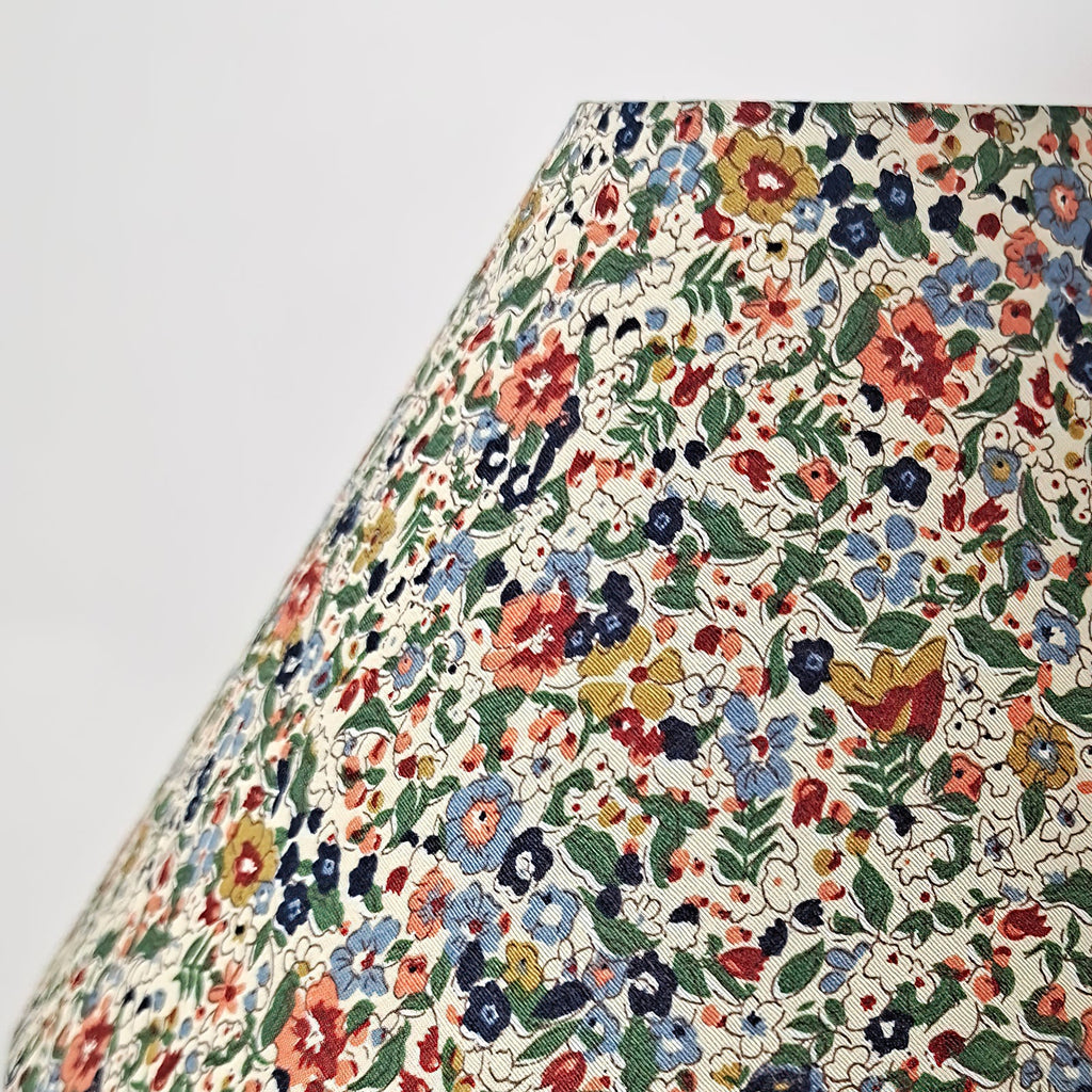 Close view of the floral fabric on the shade of this Clérachic table lamp, with blue, red and yellow flowers and green leaves on cream.