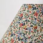 Close view of the floral fabric on the shade of this Clérachic table lamp, with blue, red and yellow flowers and green leaves on cream.