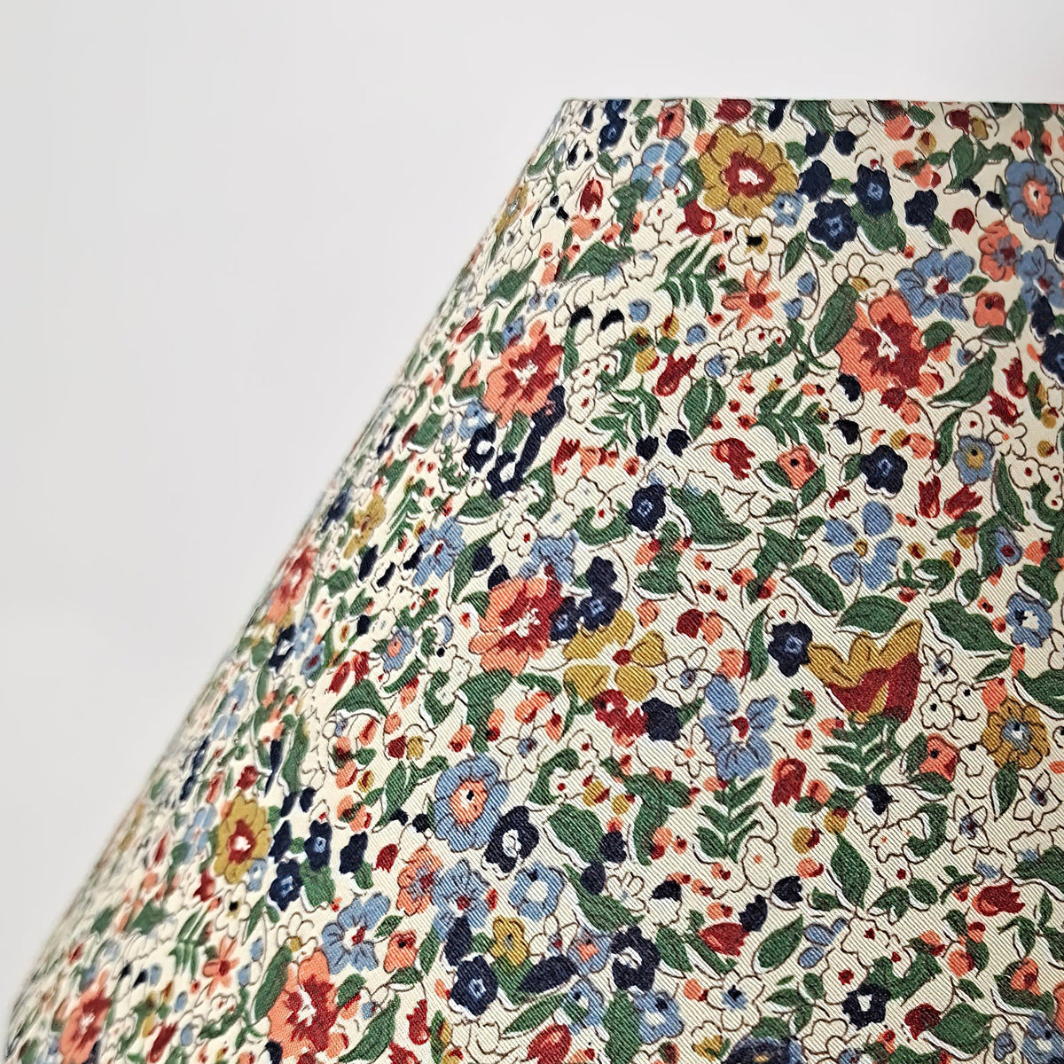 Close view of the floral fabric on the shade of this Clérachic table lamp, with blue, red and yellow flowers and green leaves on cream.