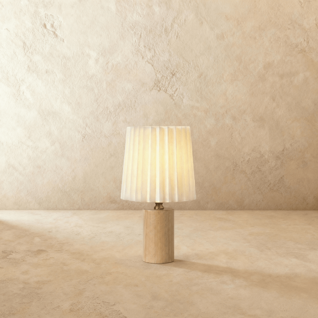 Clérachic table lamp with a pleated cream shade glowing warm above a slim light oak cylinder base on a plaster-toned backdrop.