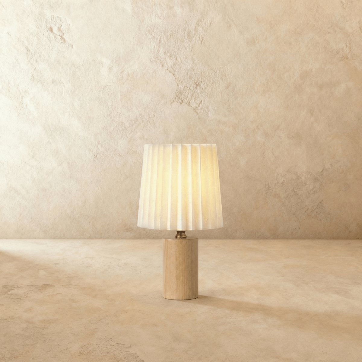 Clérachic table lamp with a pleated cream shade glowing warm above a slim light oak cylinder base on a plaster-toned backdrop.