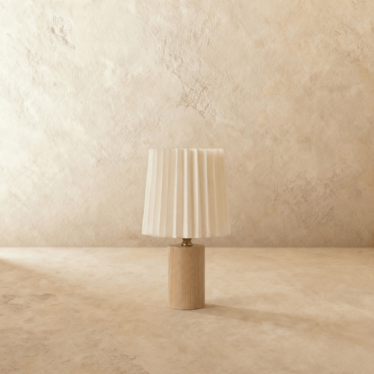 Clérachic table lamp with an unlit pleated cream shade above a light natural wood cylinder base, brass-toned neck, plaster backdrop.