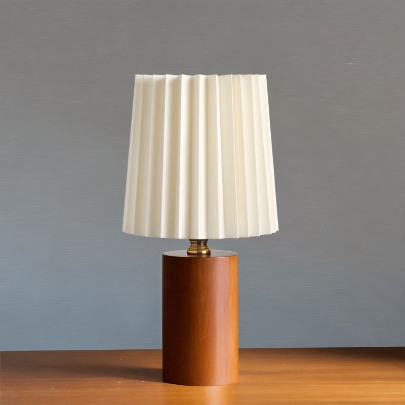 Clérachic table lamp with a pleated cream shade, brass collar and a warm walnut-toned cylinder base against a grey backdrop.