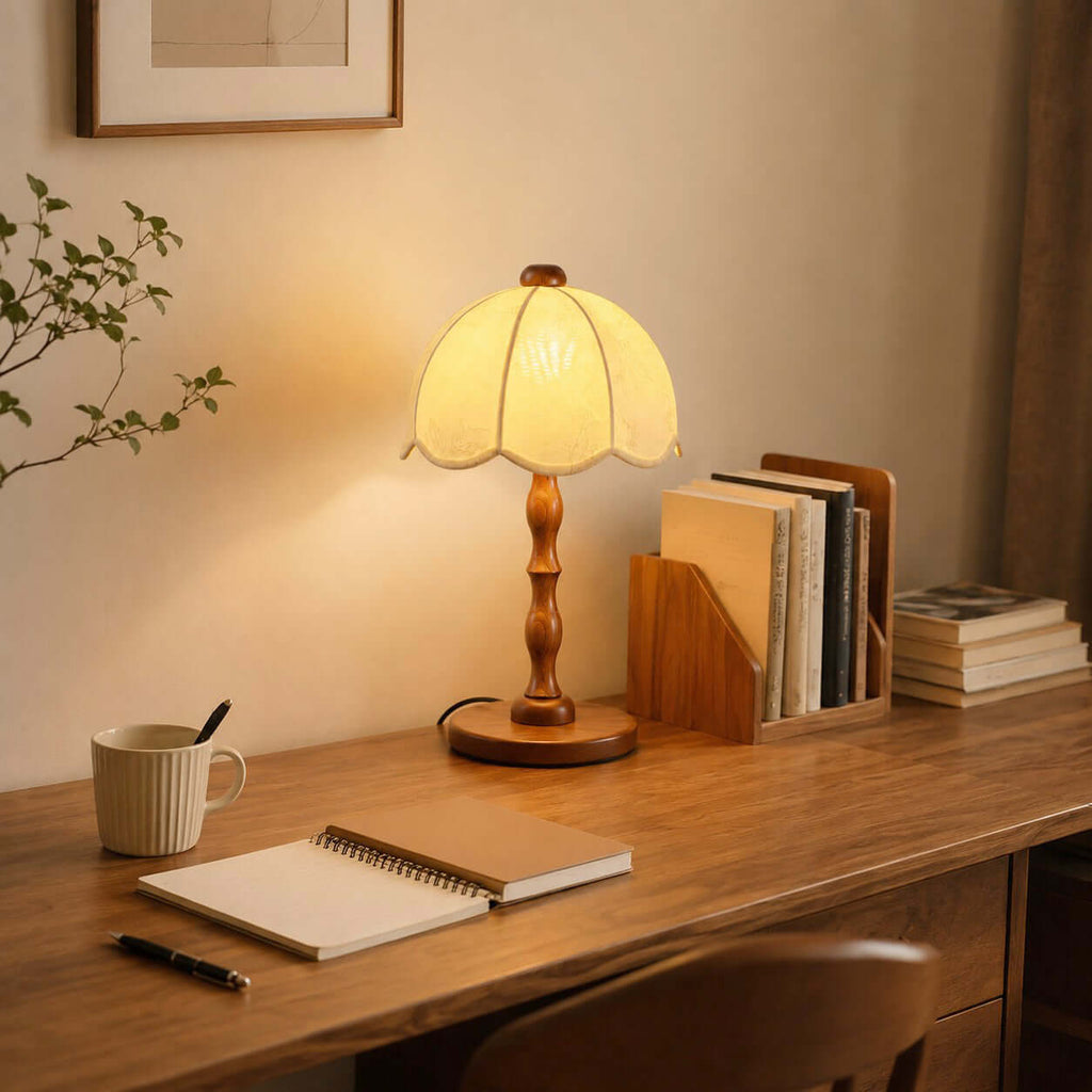 Warm glow from the scalloped shade of this Clérachic table lamp on a wooden desk with a notebook, a mug and a book rack.