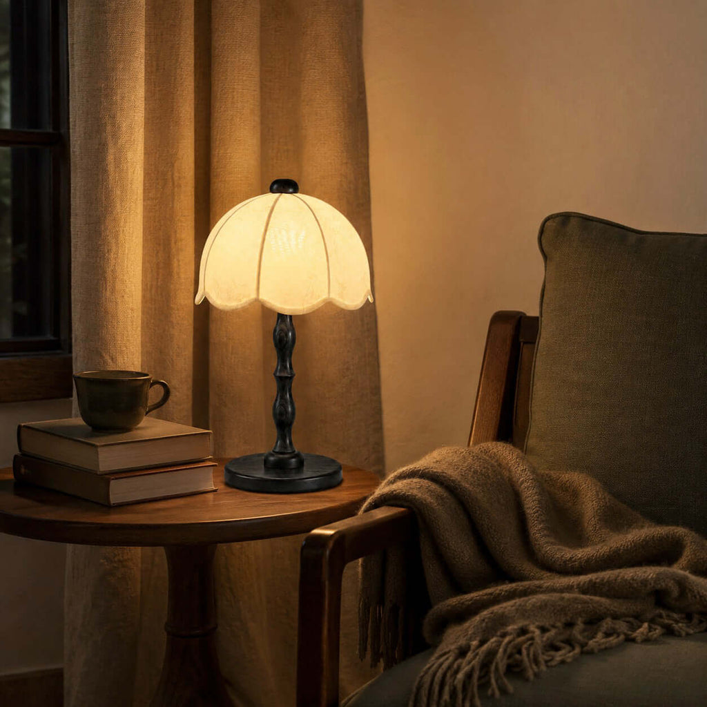 Clérachic table lamp with a black base and scalloped shade on a round side table, with a green chair and a brown throw.