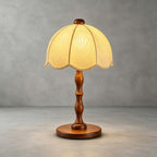 A Clérachic table lamp with a walnut turned stem and round base, lit on a concrete-grey studio backdrop.