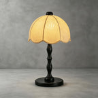 Clérachic table lamp with a black turned stem and round base, with a scalloped shade, on a concrete-grey backdrop.