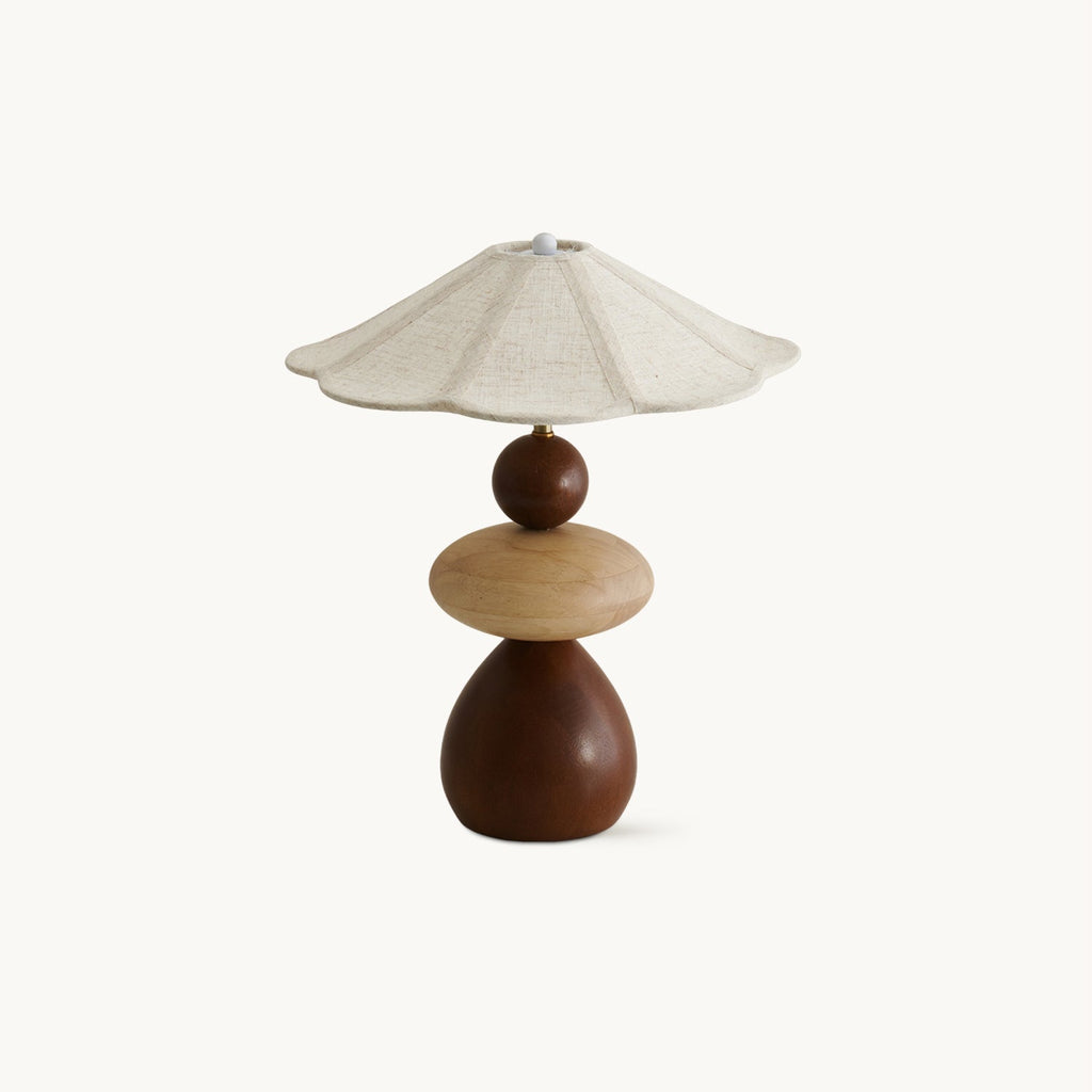 A Clérachic table lamp on a plain white backdrop, with a scalloped linen shade over stacked walnut and pale wood shapes.