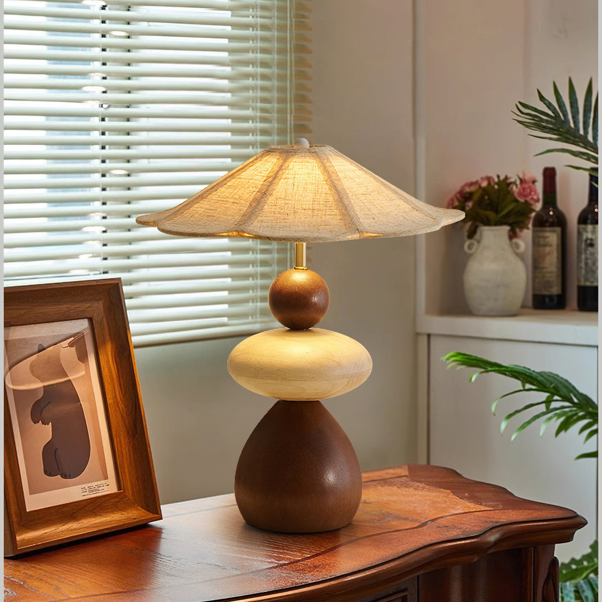 This Clérachic table lamp glows on a carved wooden console, beside a framed print and a window with white blinds.