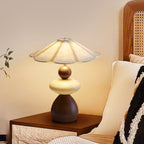 Warm light from this Clérachic table lamp falls on a cream cushion and a patterned throw, with a cane headboard behind.