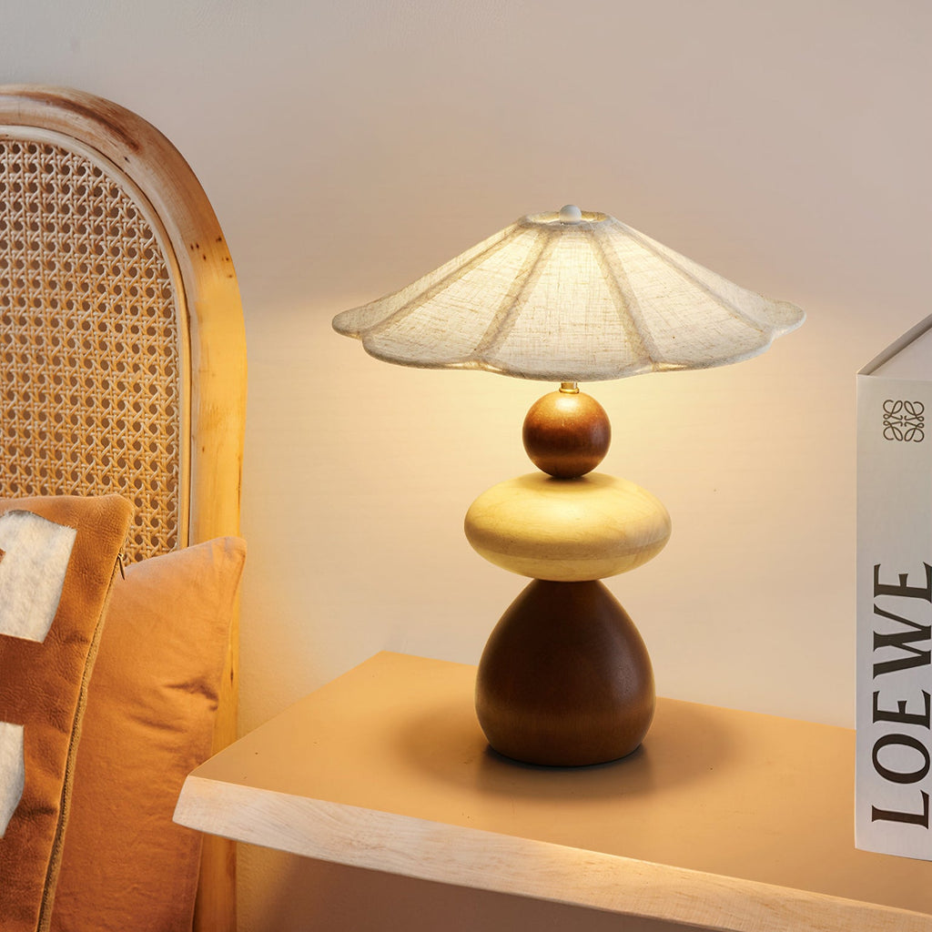 This Clérachic table lamp sits on a pale wooden shelf in front of a cane headboard, with a tan cushion at the left.