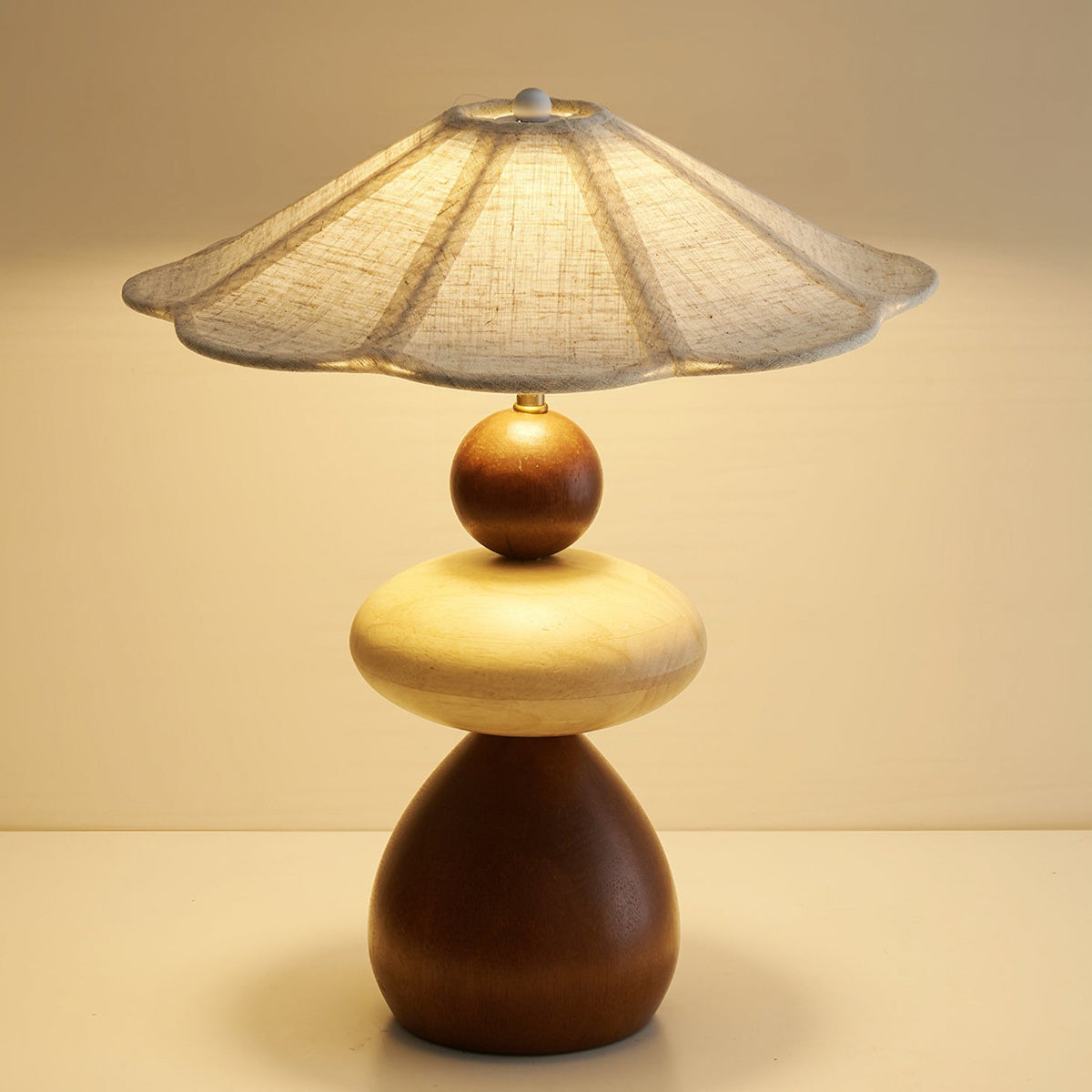 Close view of the flared linen shade and the stacked walnut and pale wood body of this Clérachic table lamp, softly lit.