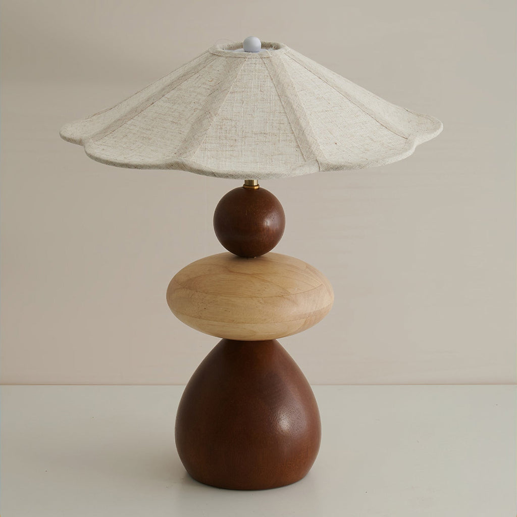 Unlit Clérachic table lamp on a grey backdrop, showing the scalloped linen shade and the three stacked wooden shapes in two tones.