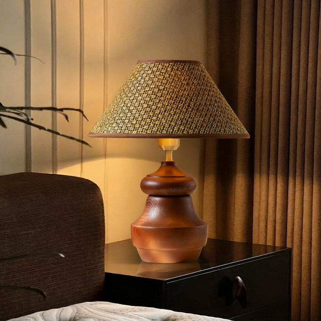 On a black bedside table beside brown curtains, a Clérachic table lamp with a straw weave shade and a rounded wood base glows.