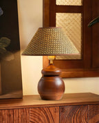 A Clérachic straw weave shade on a rounded wood base, set on a carved wooden sideboard under a lattice window.
