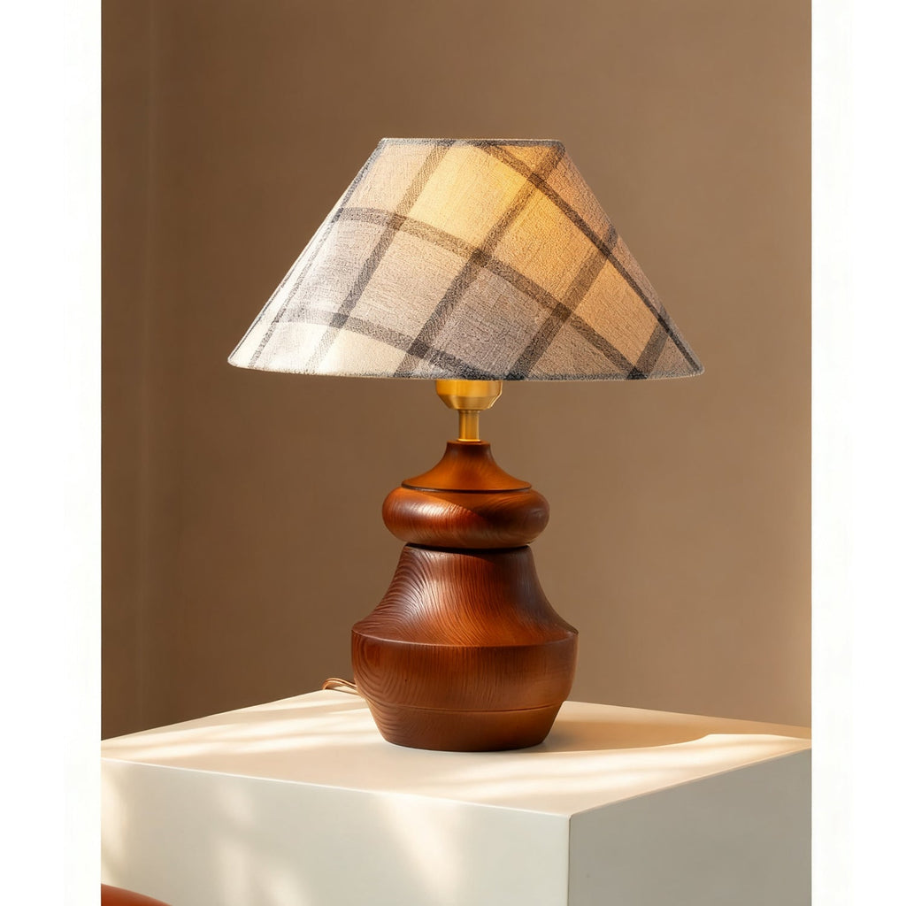 A Clérachic plaid-shade table lamp on a white plinth, with a rounded walnut-colour wood base and a brass neck.