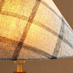 Close view of the plaid linen-look fabric on this Clérachic lamp shade, lit from within, above the brass neck.