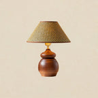 A Clérachic straw weave shade on a round-bellied wood base with a brass neck, shown on a soft beige backdrop.