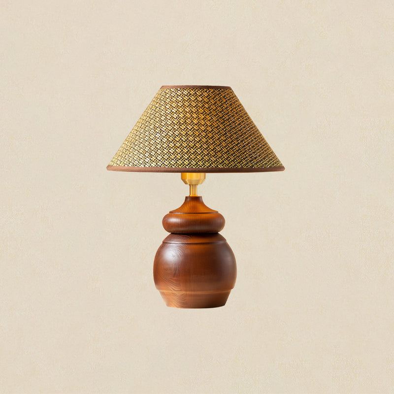 A Clérachic straw weave shade on a round-bellied wood base with a brass neck, shown on a soft beige backdrop.